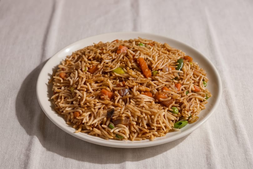 A white plate filled with vegetable fried rice, featuring carrots, peas, and green onions.