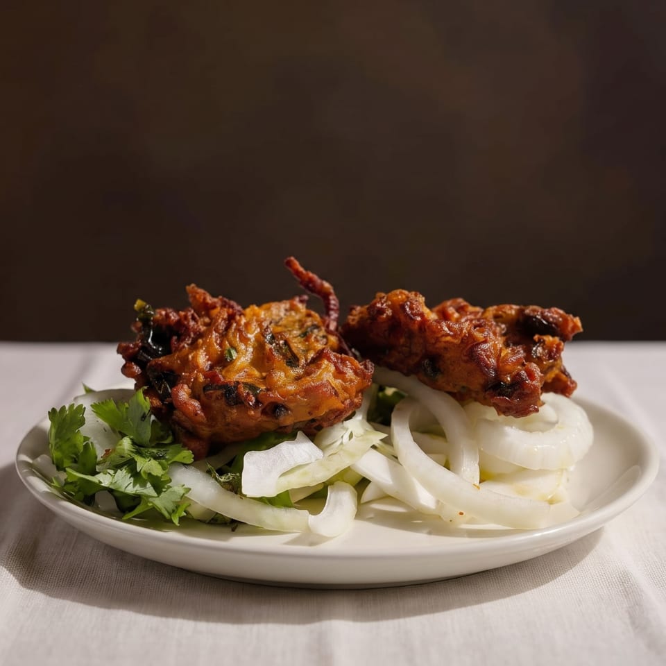 Two golden-brown pakoras, garnished with fresh cilantro and sliced onions, on a white plate.